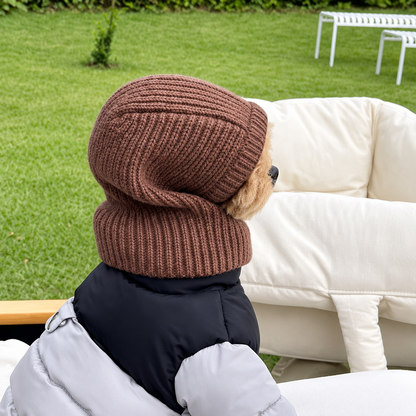 Side view of a small dog wearing a brown knitted head cover outdoors
